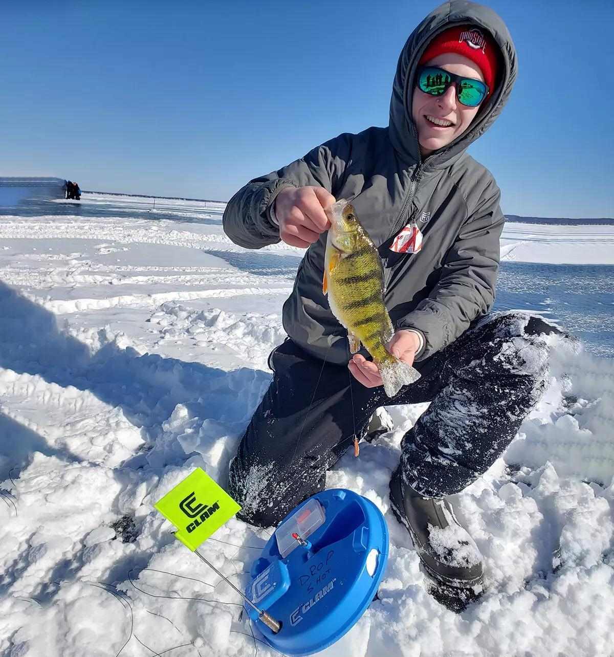 An ice angler holding a yellow perch over a blue tip-up.